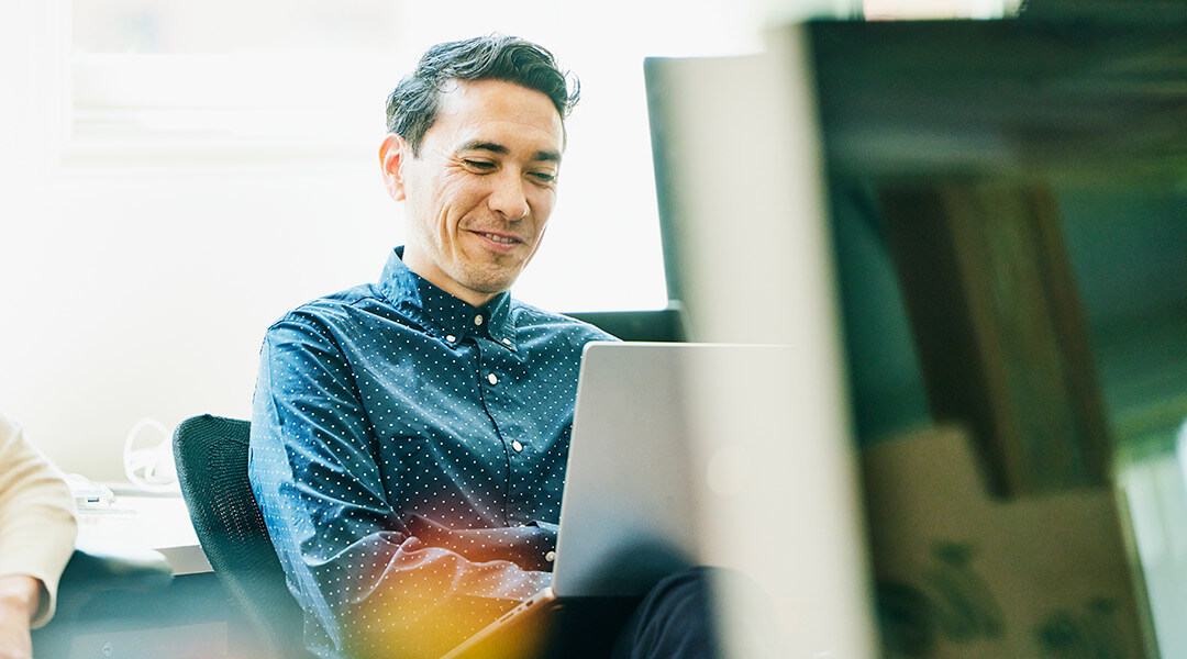 Person smiling while working with a laptop, suggesting financial planning.